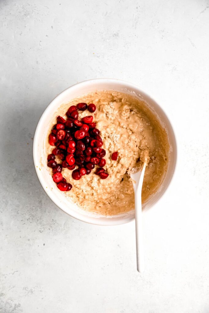 cranberries added to the bowl with the protein muffin batter; there is a wooden spoon in the bowl.