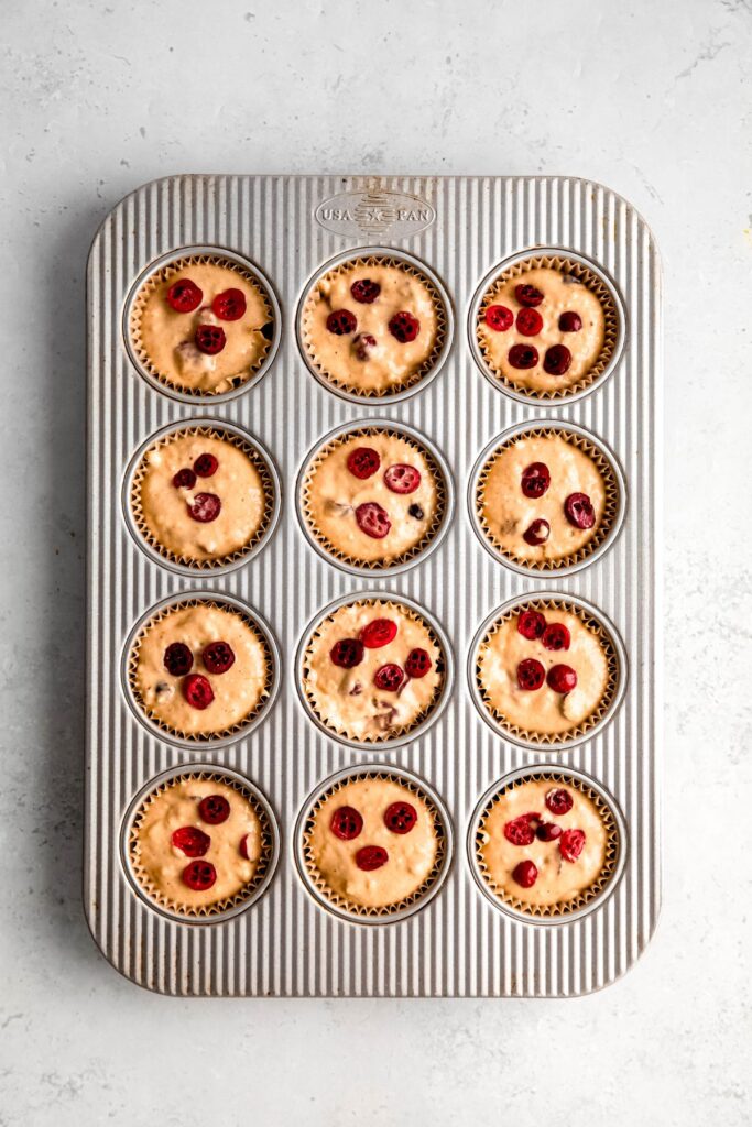 muffin batter divvied up between 12 paper muffin cup lined wells of a muffin tin and topped with extra cranberries.