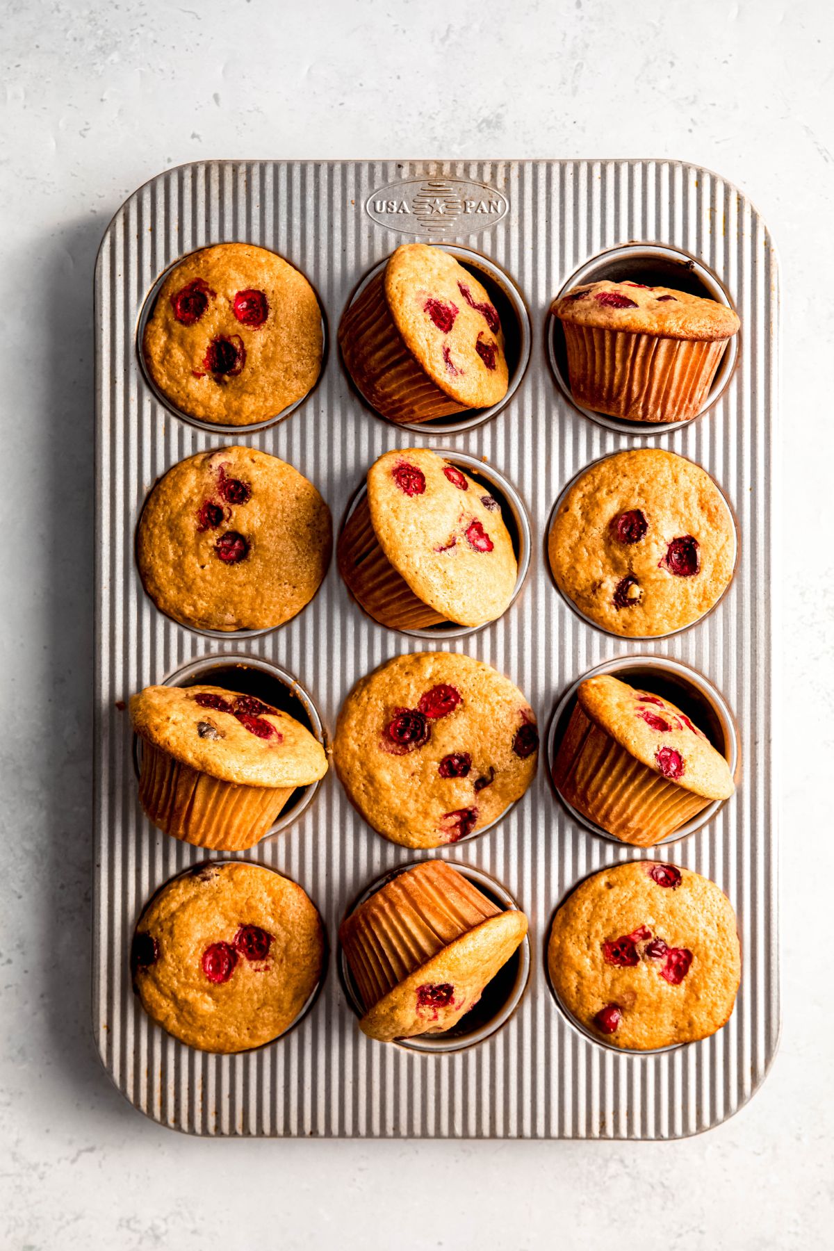 baked orange cranberry protein muffins in the muffin tin with some tilted on their side.