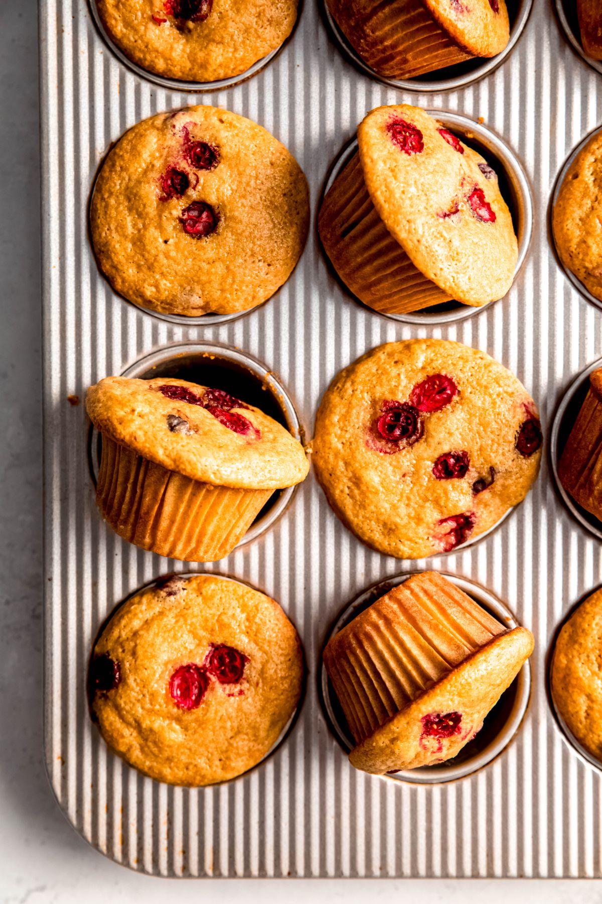 overhead closeup shot of cranberry orange protein muffins in a striped silver muffin tin with every other muffin tilted on its side.