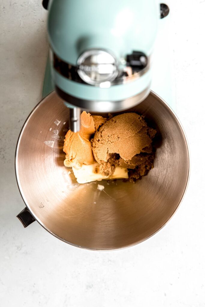 butter, peanut butter, and brown sugar added to the mixing bowl of a pale blue stand mixer.