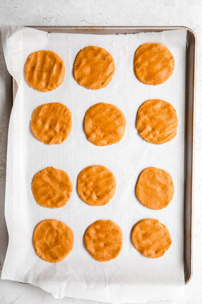 12 flattened rounds of peanut butter cookie dough on a parchment lined baking sheet.