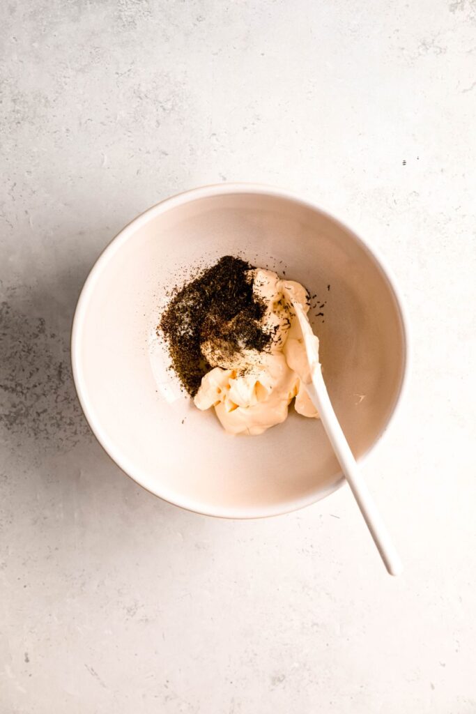 mayo, lemon juice, and seasonings added to a mixing bowl with a wooden spoon.