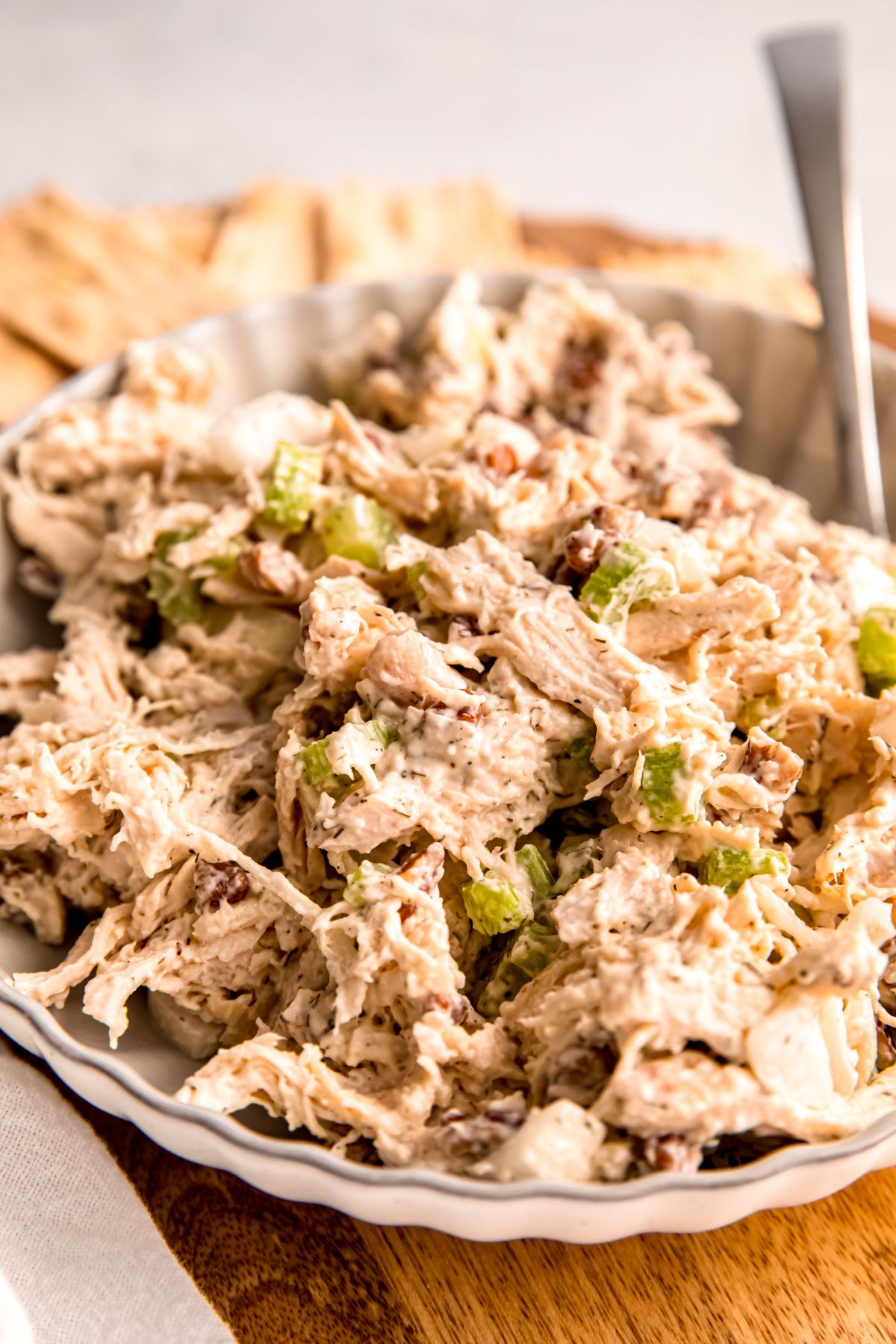 closeup shot of a white bowl of leftover turkey salad sandwich filling on a wooden cutting board; you can see the shreds of turkey, chopped nuts, and chunks of crunchy celery.
