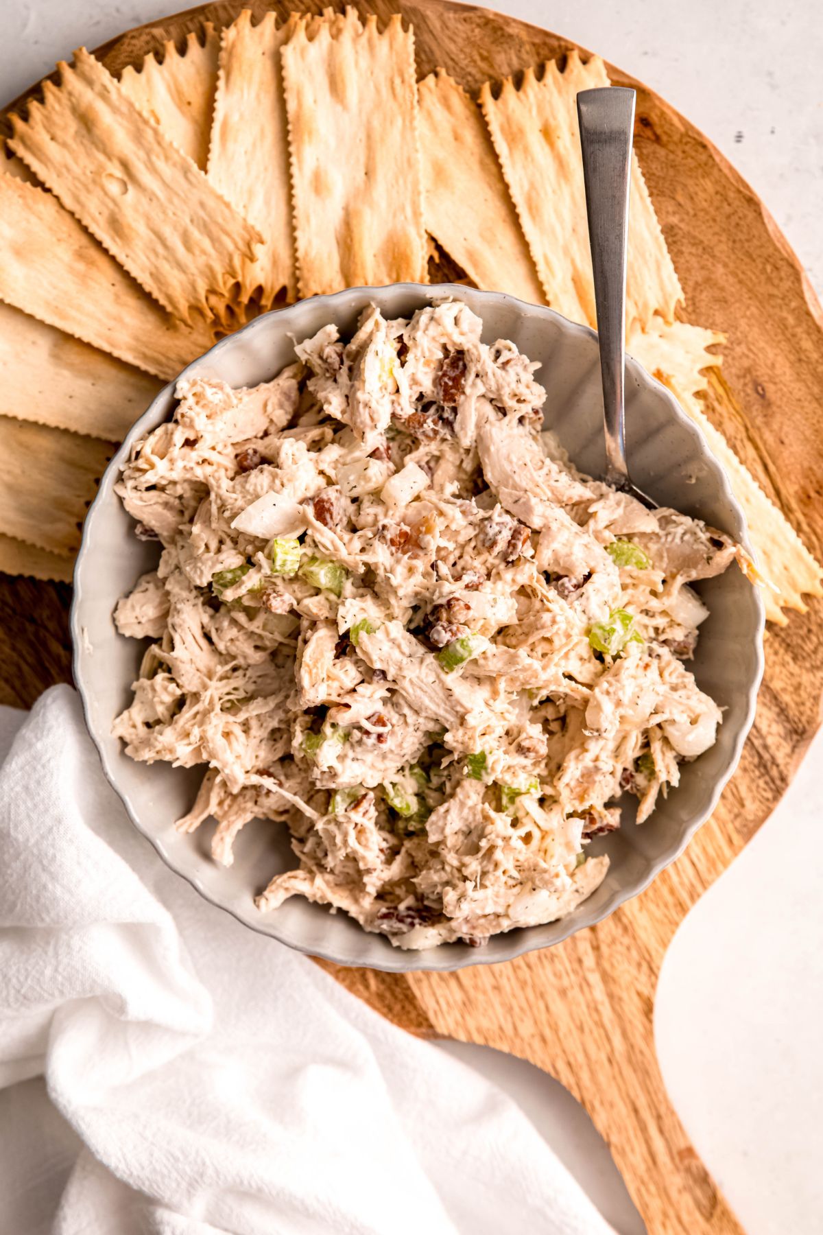 overhead shot of creamy turkey salad sandwich filling in a white bowl on a wooden board with crackers for serving.