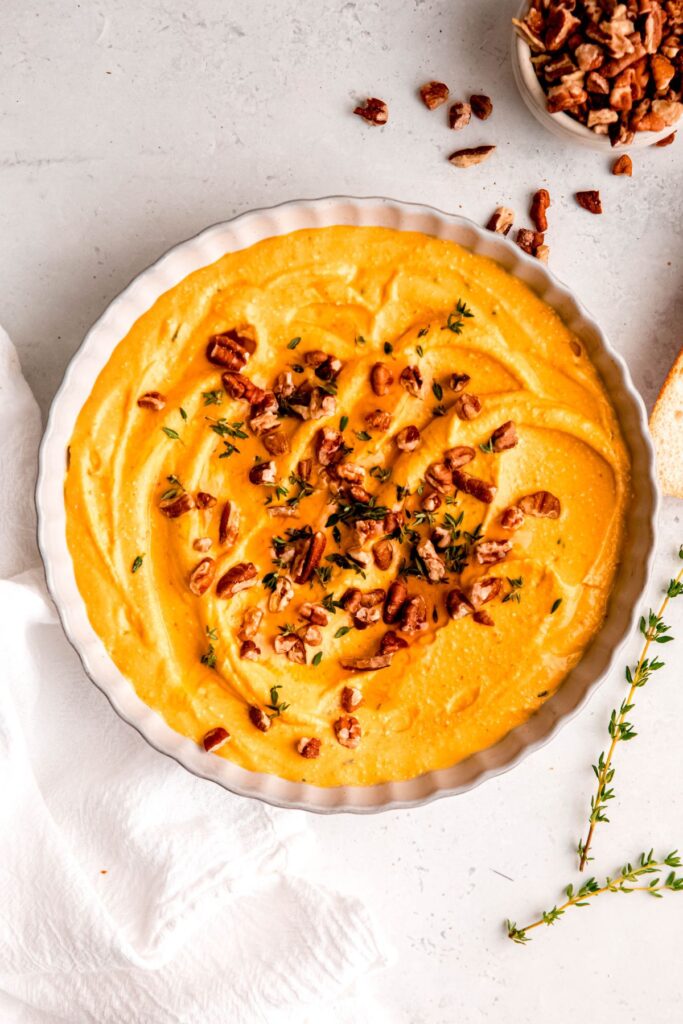 An overhead shot of a bowl of the pumpkin whipped feta next to a small dish of pecans.