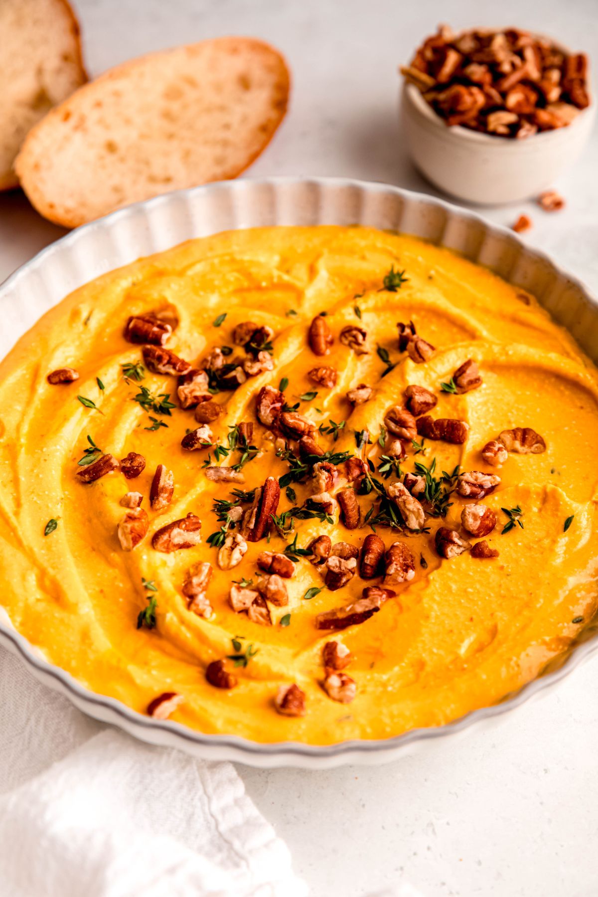 A close-up angled shot of a bowl of pumpkin whipped feta dip, topped with nuts and herbs.