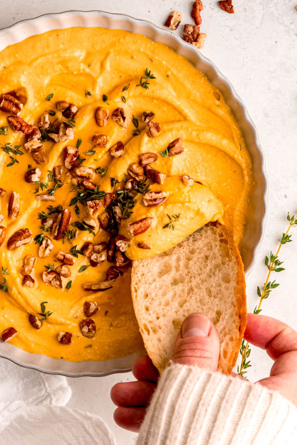 A close-up overhead shot of a serving bowl of pumpkin whipped feta with a baguette dipped in it.