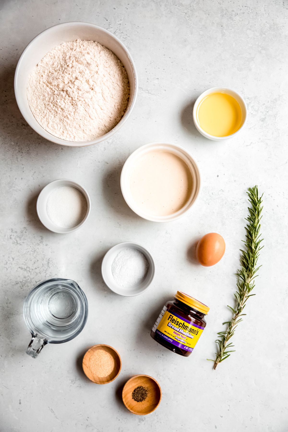 ingredients needed to make sourdough discard dinner rolls with rosemary and garlic measured out on a white table.