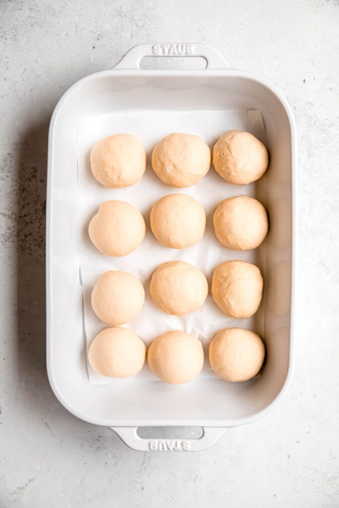 12 balls of dough set in a parchment lined 9x13 casserole dish for proofing.