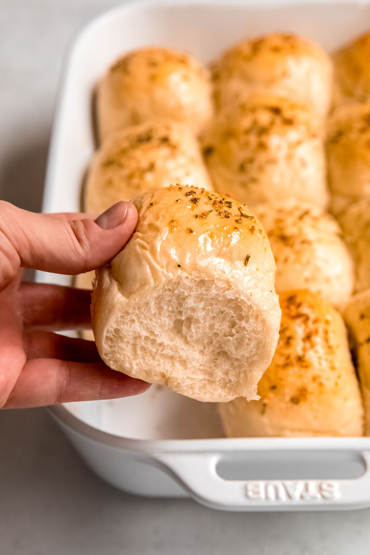 hand grabbing the left front corner sourdough discard roll topped with rosemary and garlic from the pan, showing the light and fluffy crumb.
