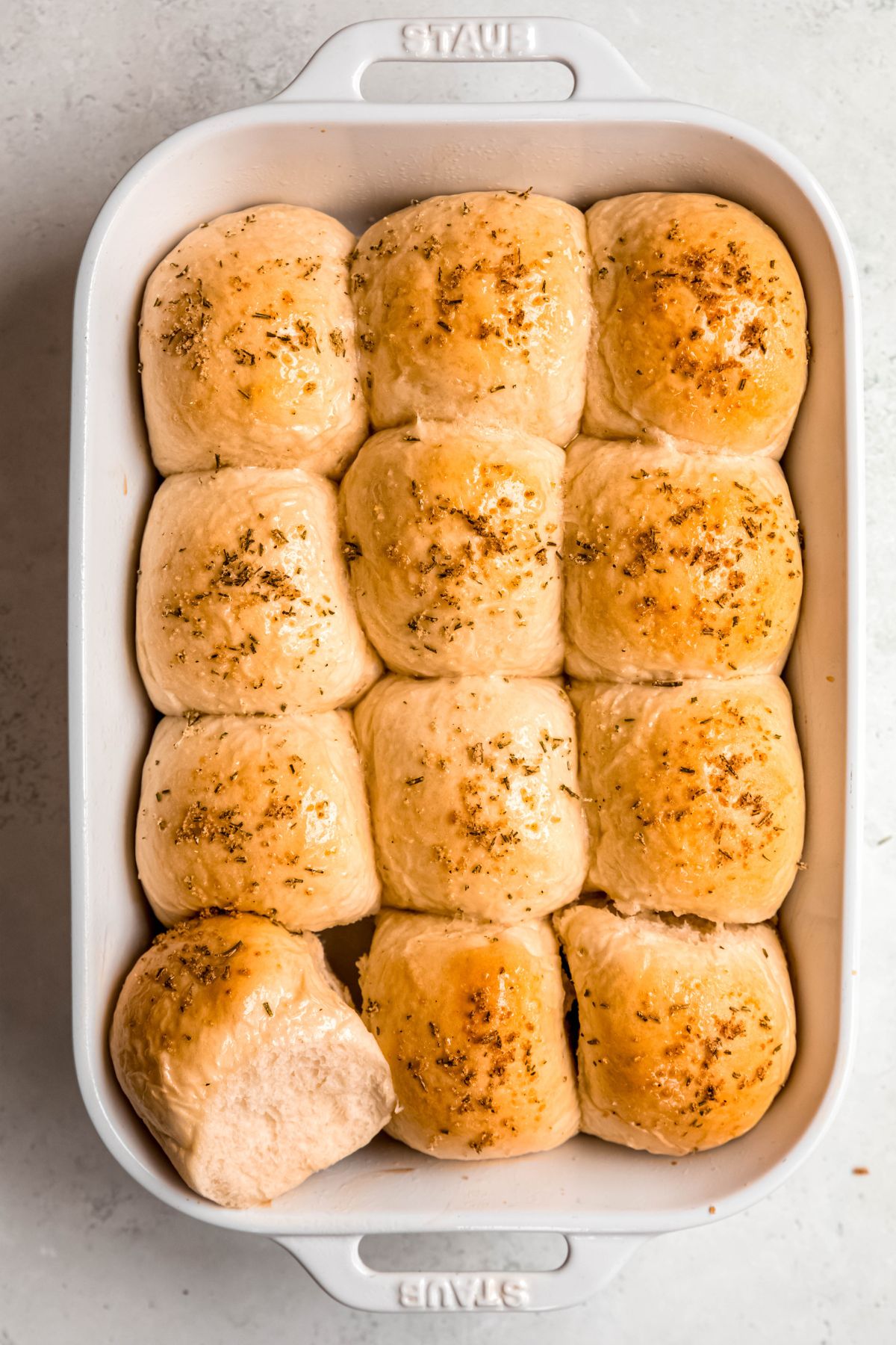 tear and share soft sourdough discard rolls in a white baking pan with the left bottom corner piece torn away and tipped on its side to show the consistency of the rolls.