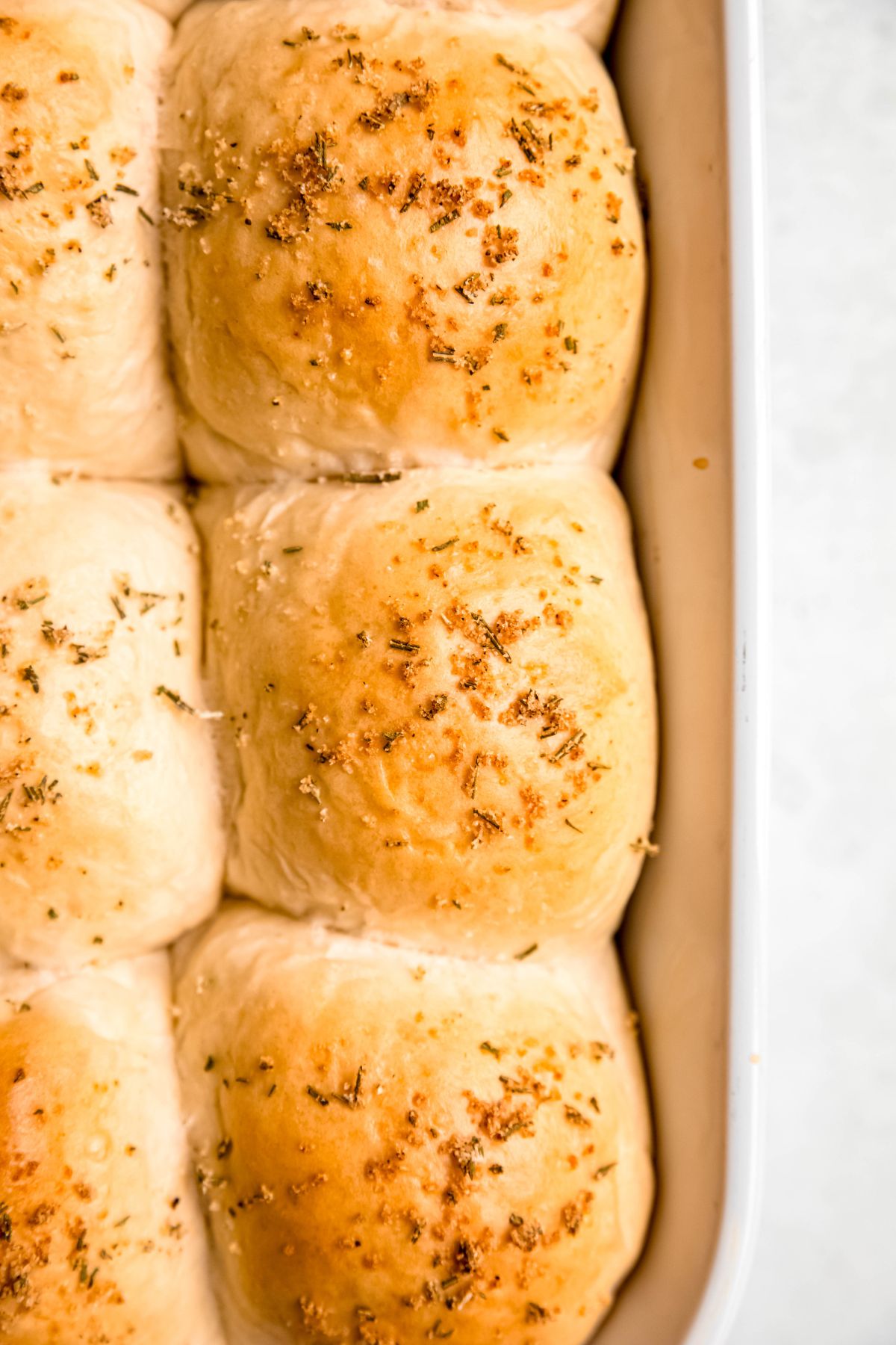 flat lay shot of the right half of a white 9x13 filled with baked rosemary garlic soft sourdough discard rolls.