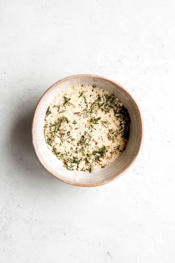parmesan cheese, fresh herbs, garlic powder, and salt mixed together in a white ceramic bowl.