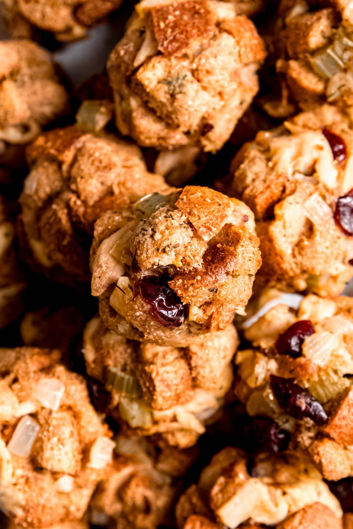 closeup overhead shot of a pile of cranberry turkey stuffing balls showing their texture—you can see the cubed bread, shredded meat, dried cranberries, and sauteed veggies.