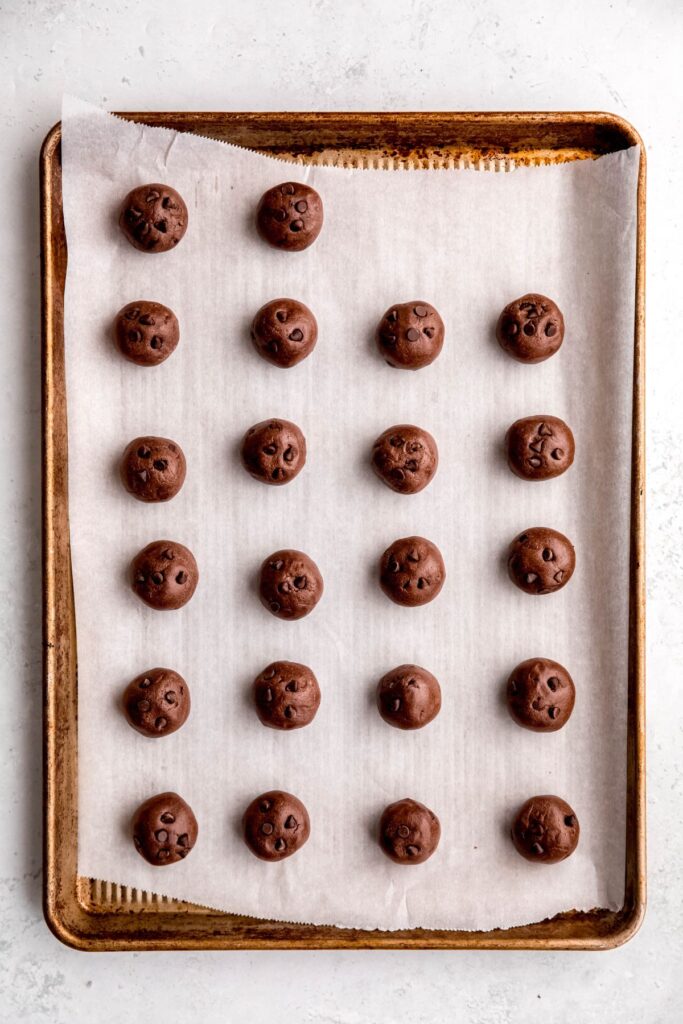parchment lined baking sheet with 18 chocolate chocolate chip protein balls lined up in rows.