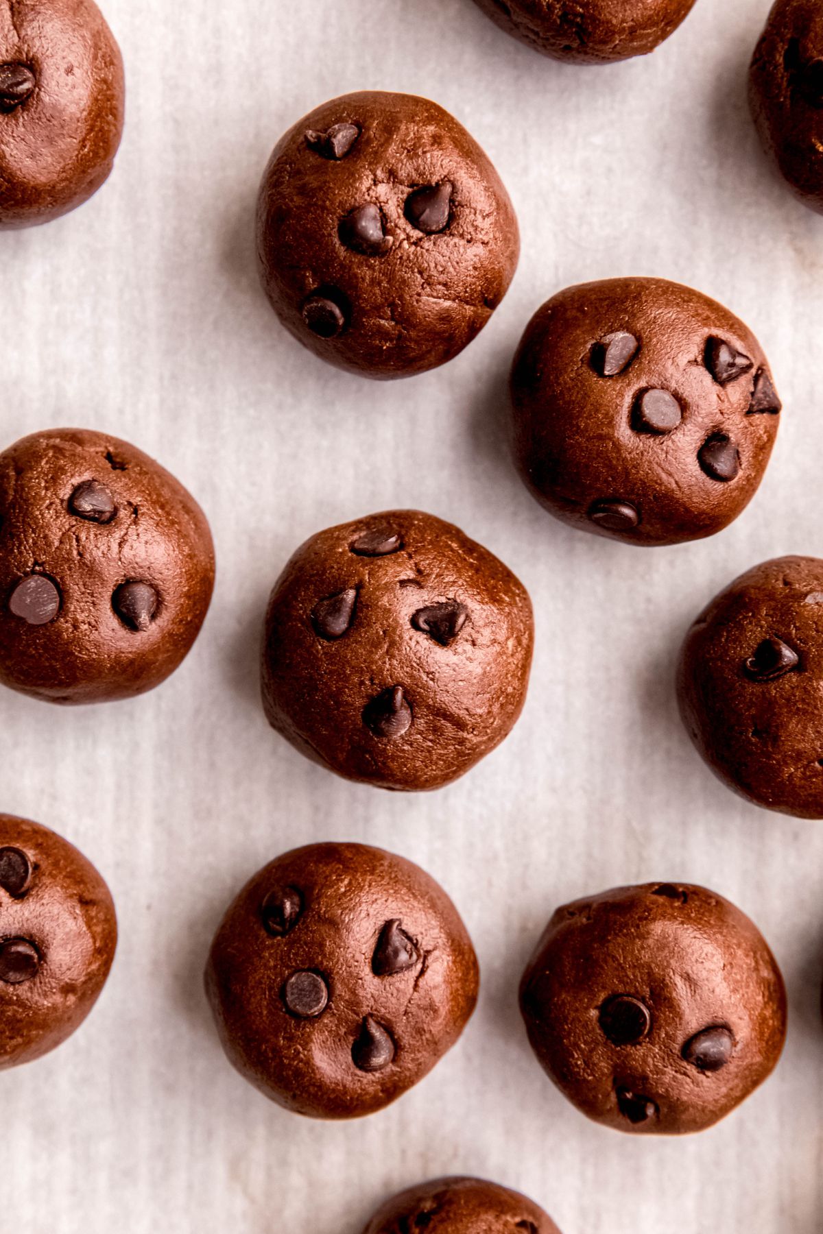overhead shot of chocolate protein balls with chocolate chips on a parchment lined baking sheet.