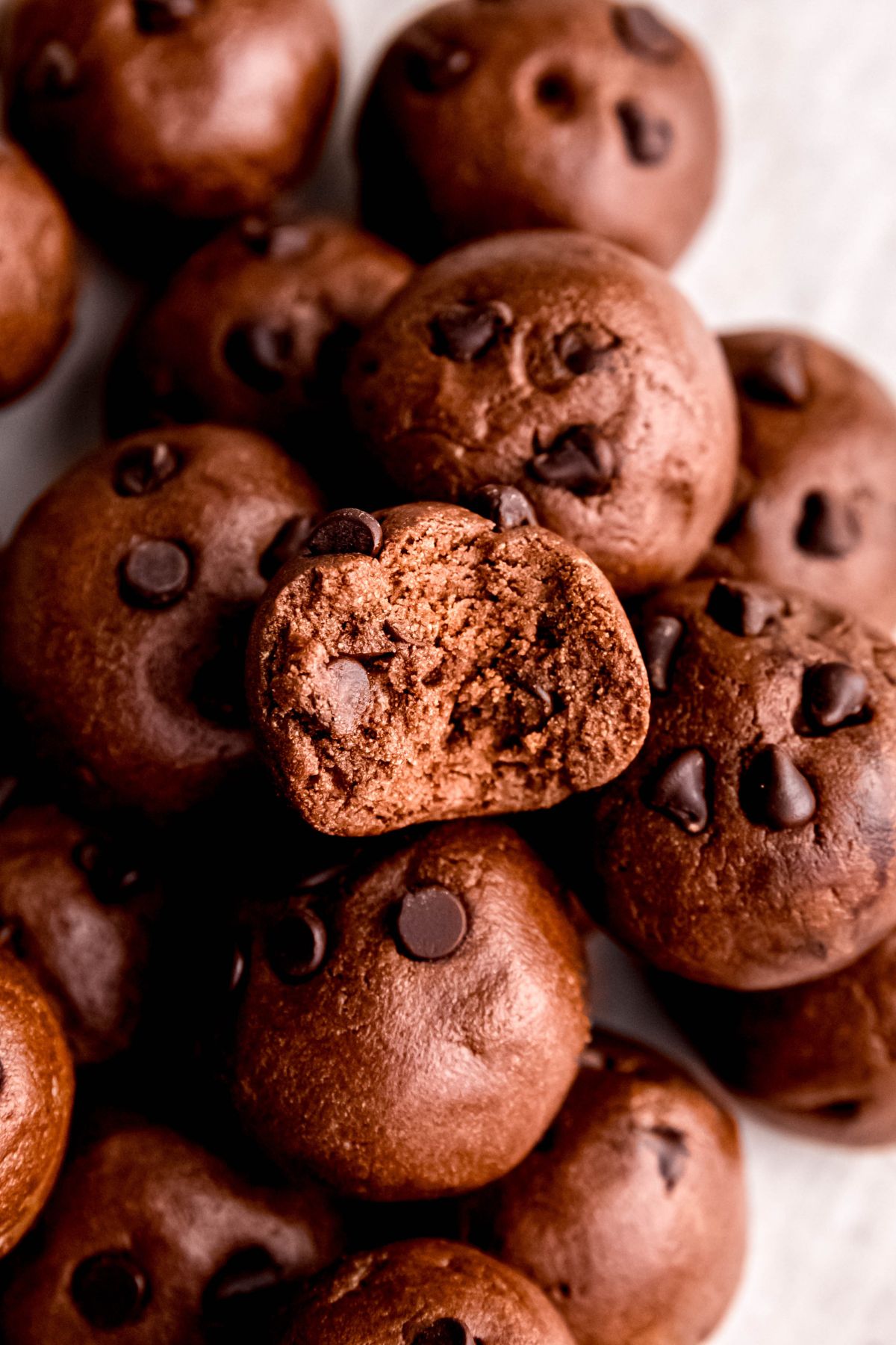 closeup overhead shot of a pile of chocolate chocolate chip protein balls with the one on top having a bite taken out of it to show the fudgy interior.