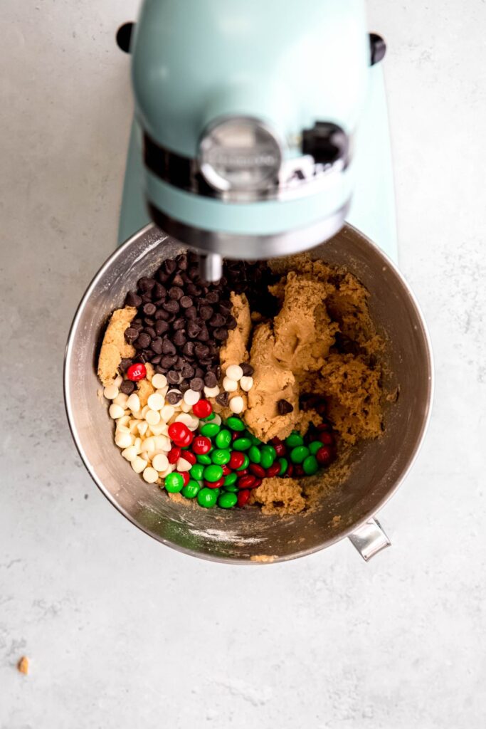 dark chocolate chips, white chocolate chips, and red and green M&Ms added to the bowl with the cookie dough.
