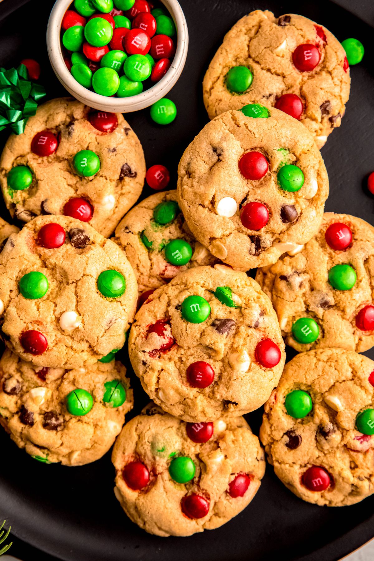 vertically framed hero shot of Christmas chocolate chip cookies with red and green m&ms and both dark and white chocolate chips on a black plate.