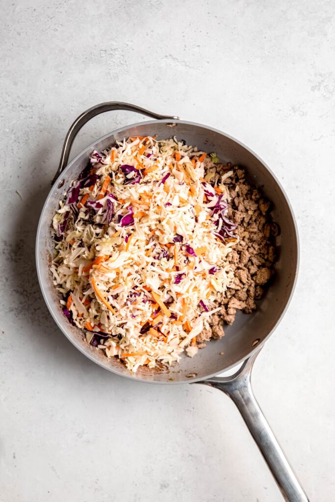 Adding the coleslaw mix to the pan of browned turkey and spices.