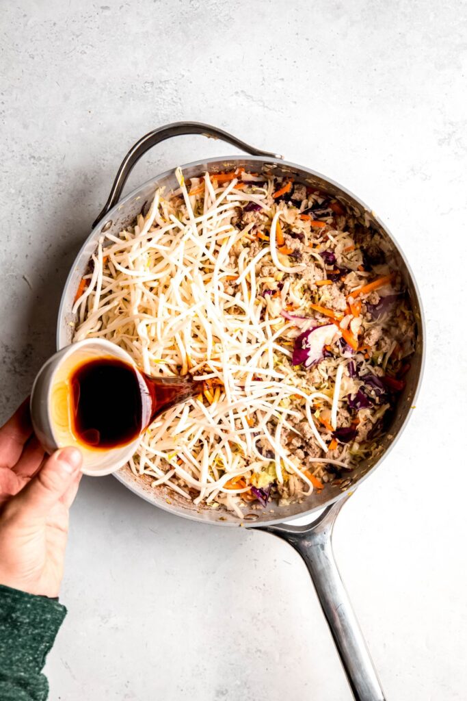 Pouring the stir fry sauce into the skillet with the bean sprouts.
