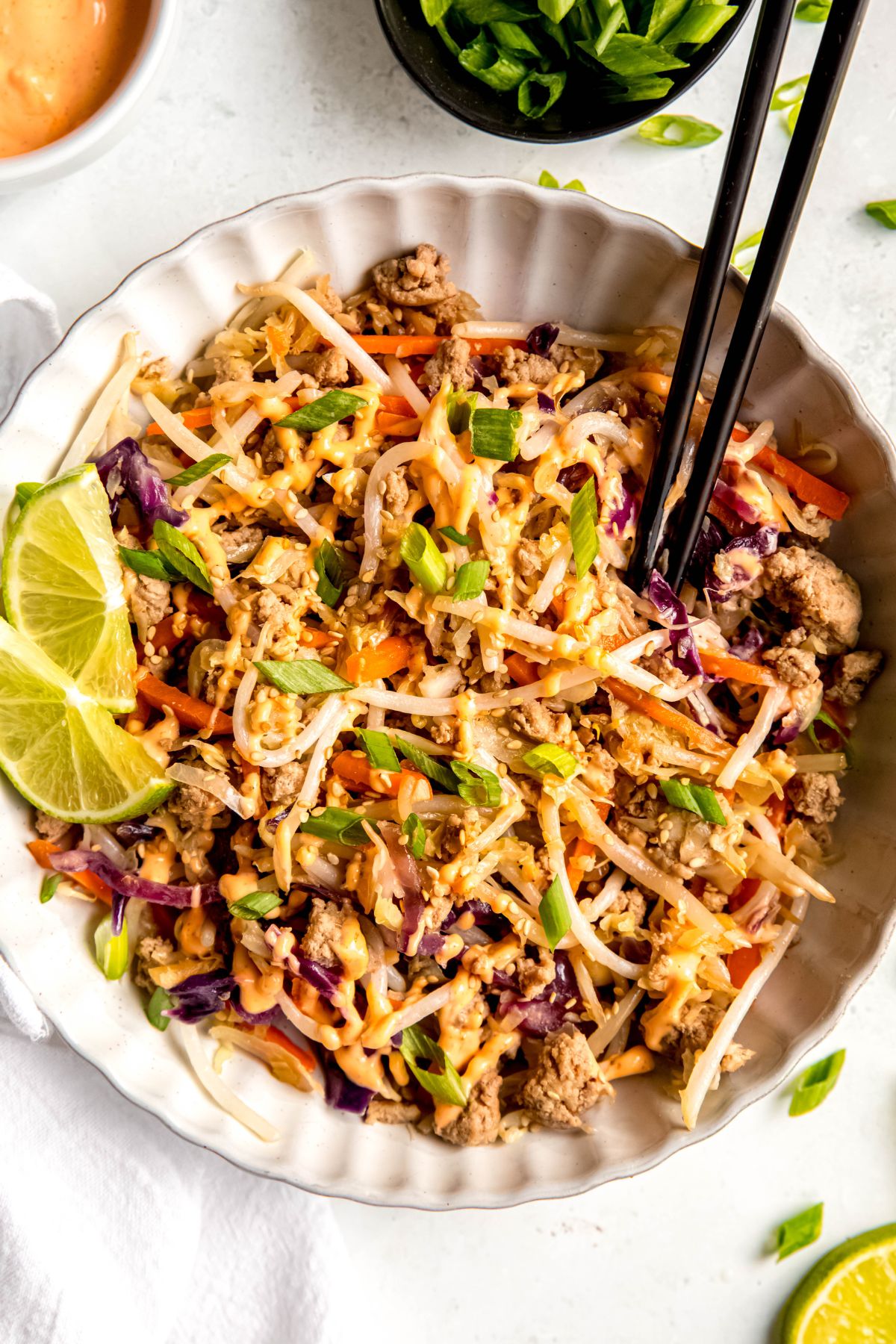 An overhead shot of egg roll in a bowl with black chopsticks and 2 lime slices.