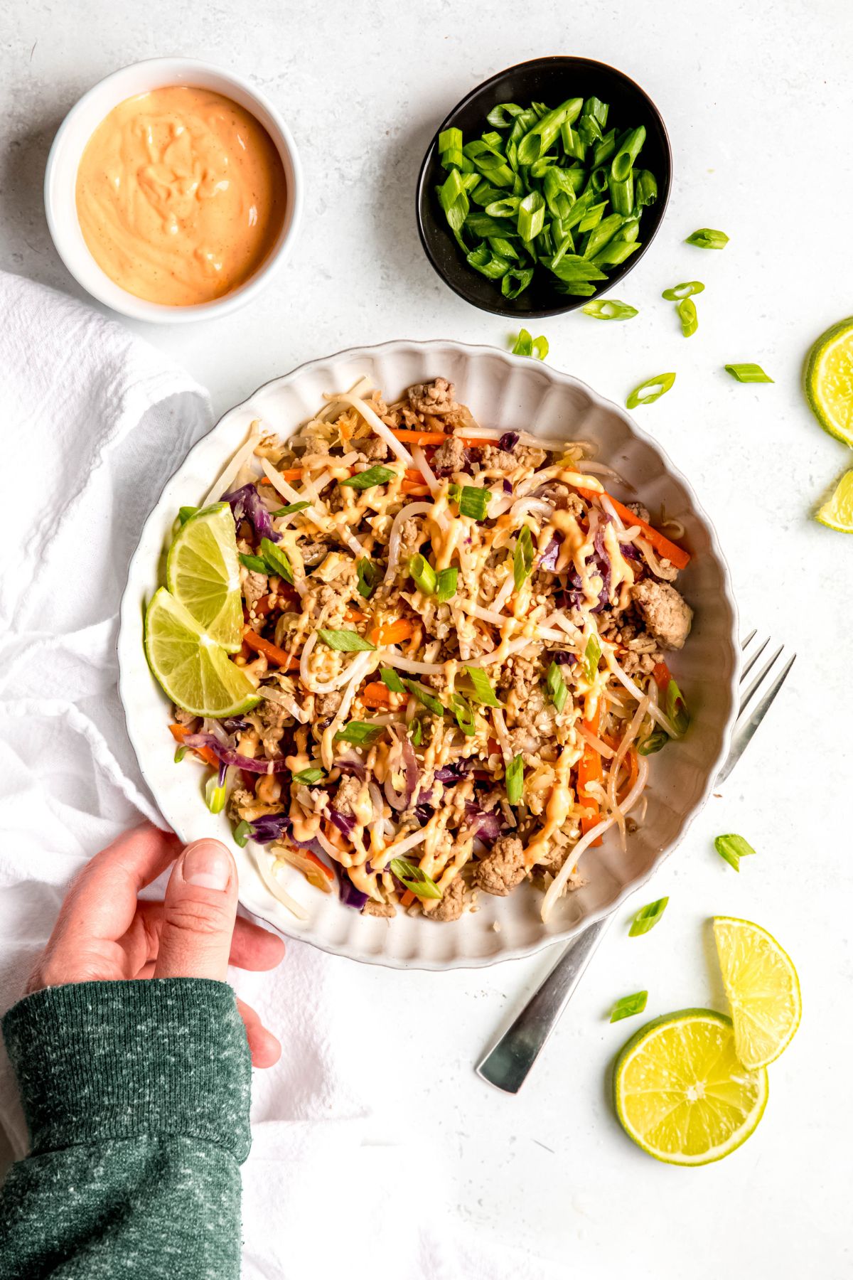An overhead shot of a hand holding a dinner plate of egg roll in a bowl, garnished with green onions and spicy mayo.