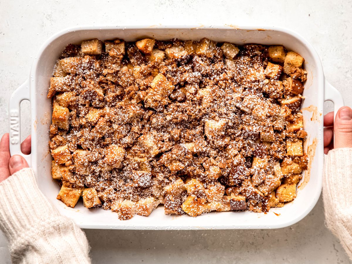 An overhead shot of two hands holding a pan of the eggnog French toast casserole.