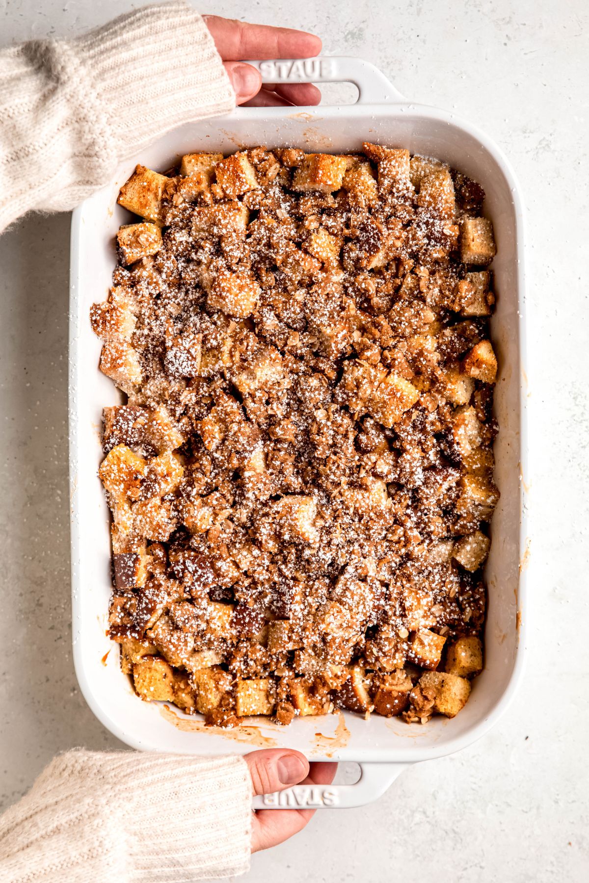 An overhead shot of two hands holding the casserole pan of eggnog french toast casserole.