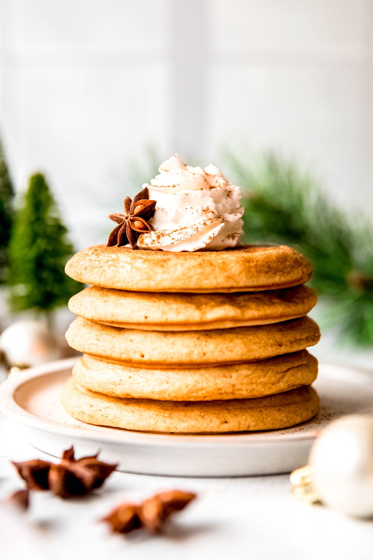 side on view of a short stack of homemade eggnog pancakes topped with whipped cream, a sprinkle of cinnamon, and a whole star anise pod leaning against the whipped cream.