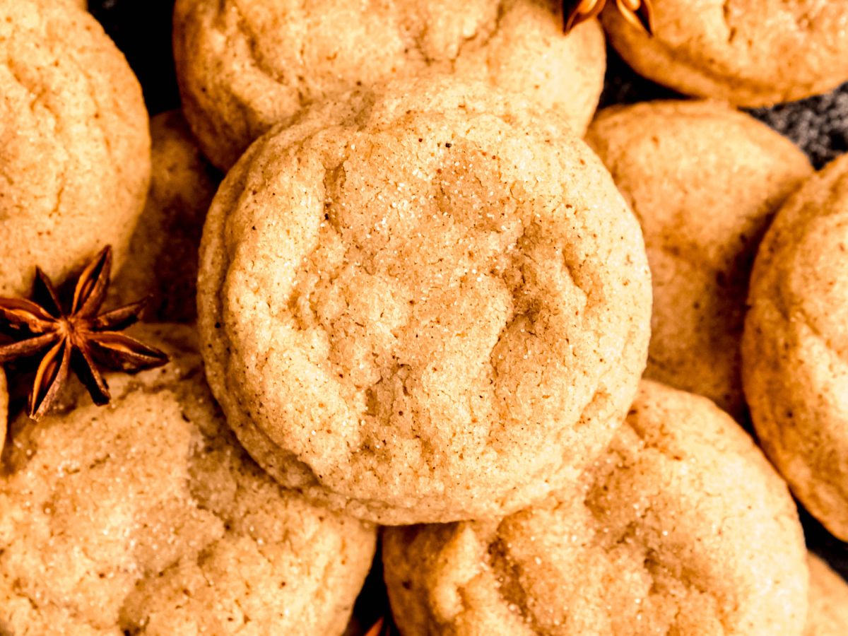 horizontally framed closeup overhead shot of a jumble of eggnog snickerdoodles on a black plate with whole star anise pods scattered around.