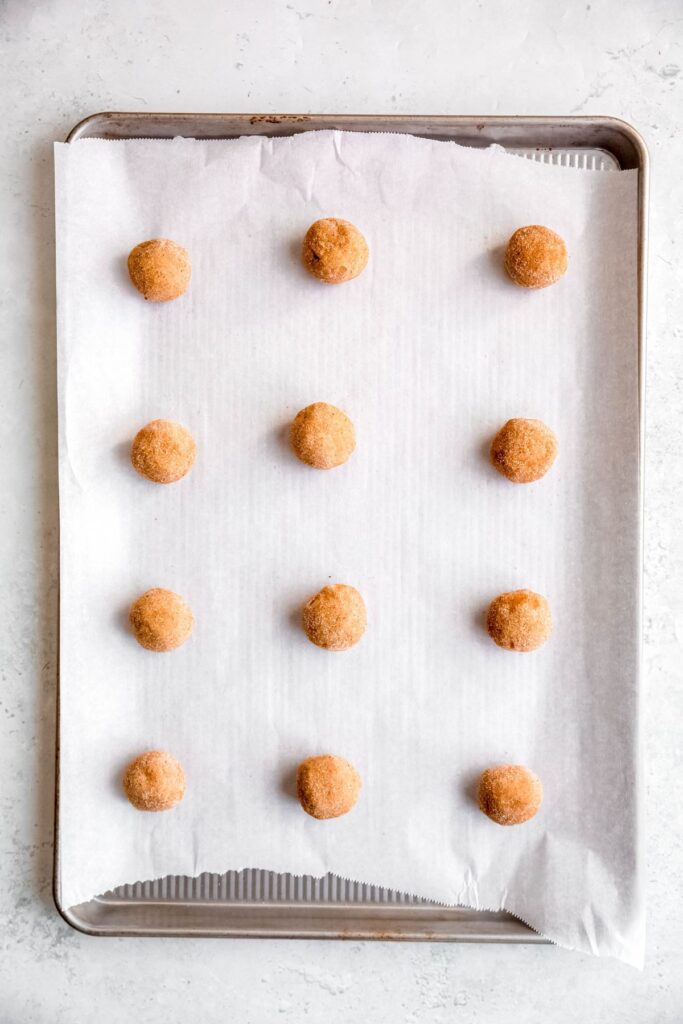 12 balls of spice-sugar rolled cookie dough balls on a parchment lined baking sheet.