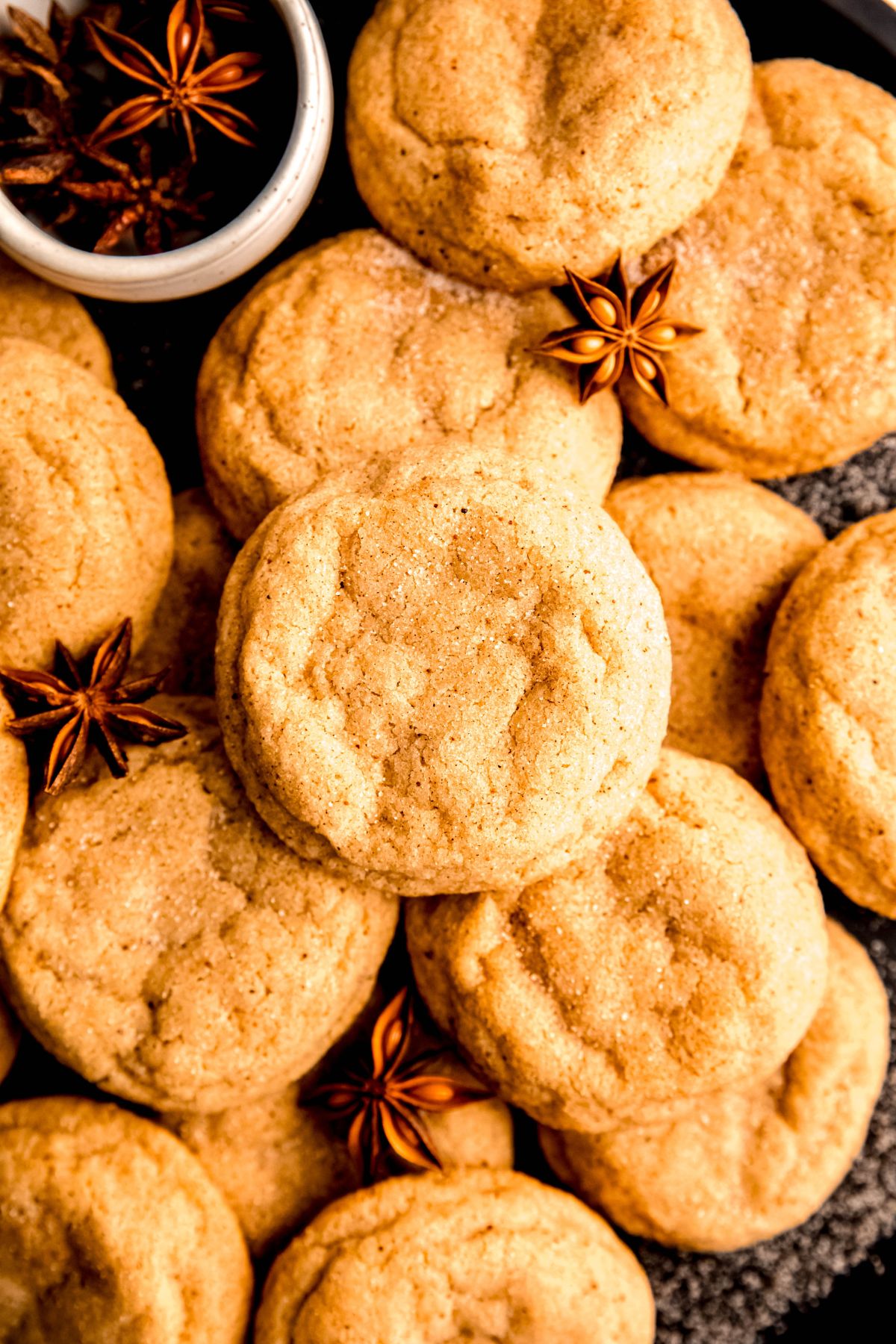 closeup overhead shot of a plate of eggnog snickerdoodles on a black plate with extra cinnamon sugar and whole star anise pods.