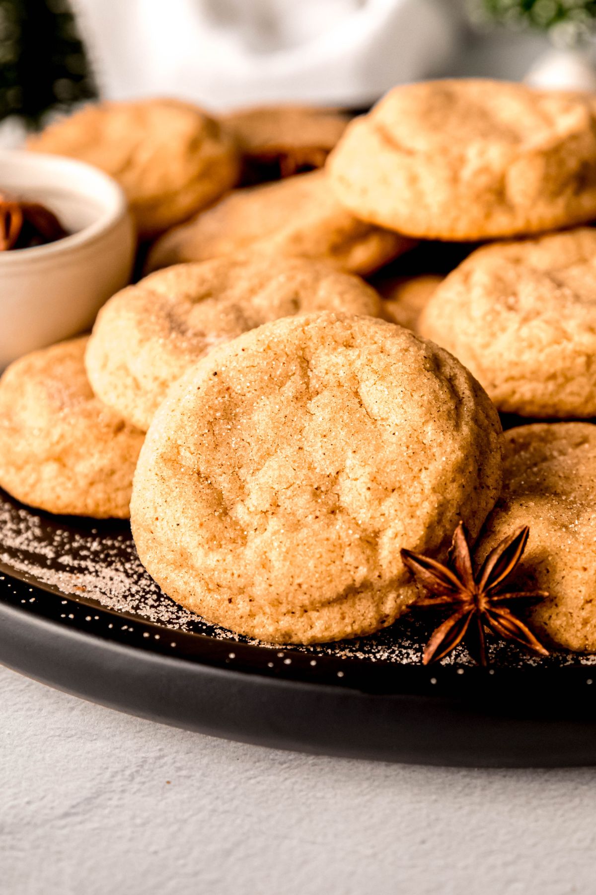 side-on view of egg nog snickerdoodles on a black plate with cinnamon sugar and whole star anise pods; you can see the sparkly coating and pale golden edges of the cookies.