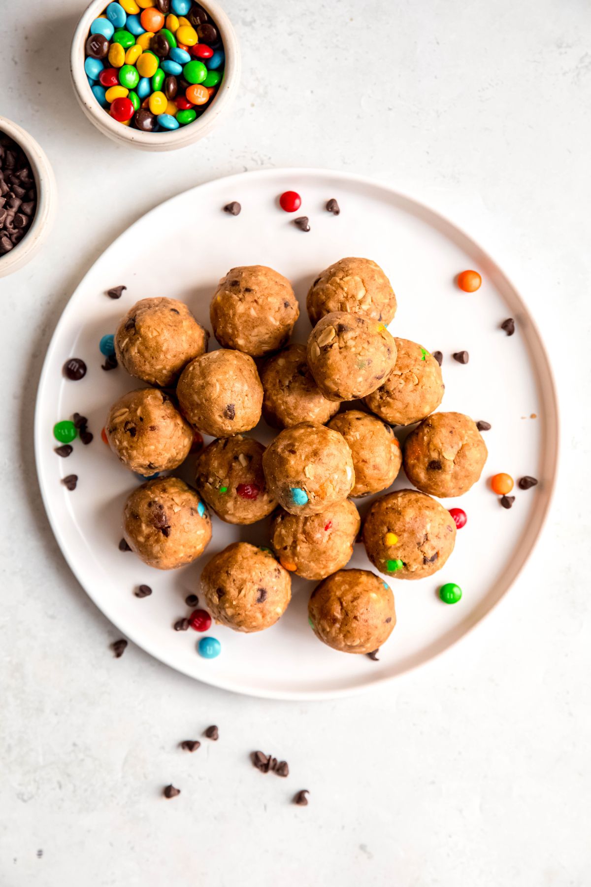 overhead shot of a white round plate with a pile of monster cookie protein balls with extra mimi M&Ms and mini chocolate chips scattered around.