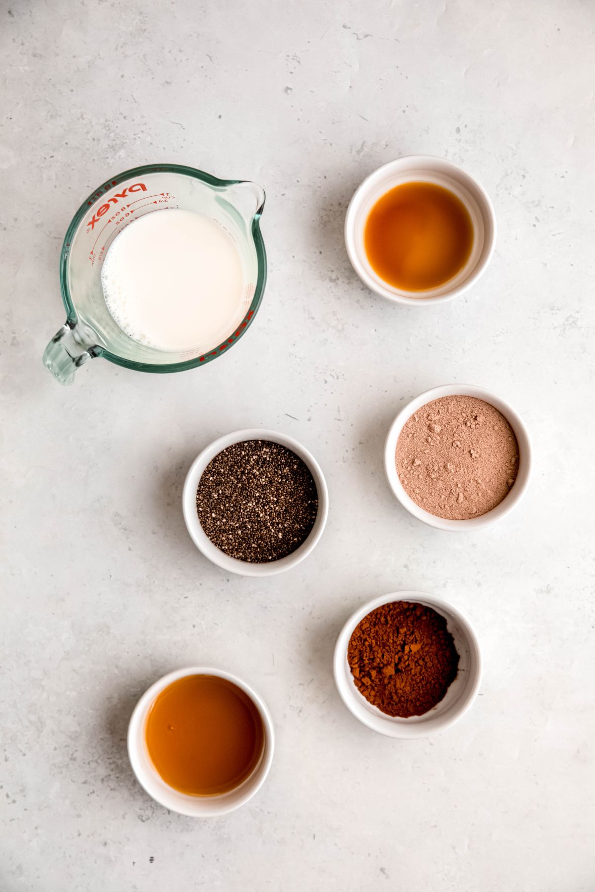overhead shot of ingredients needed to make high protein chocolate chia seed pudding recipe measured out on a white table.