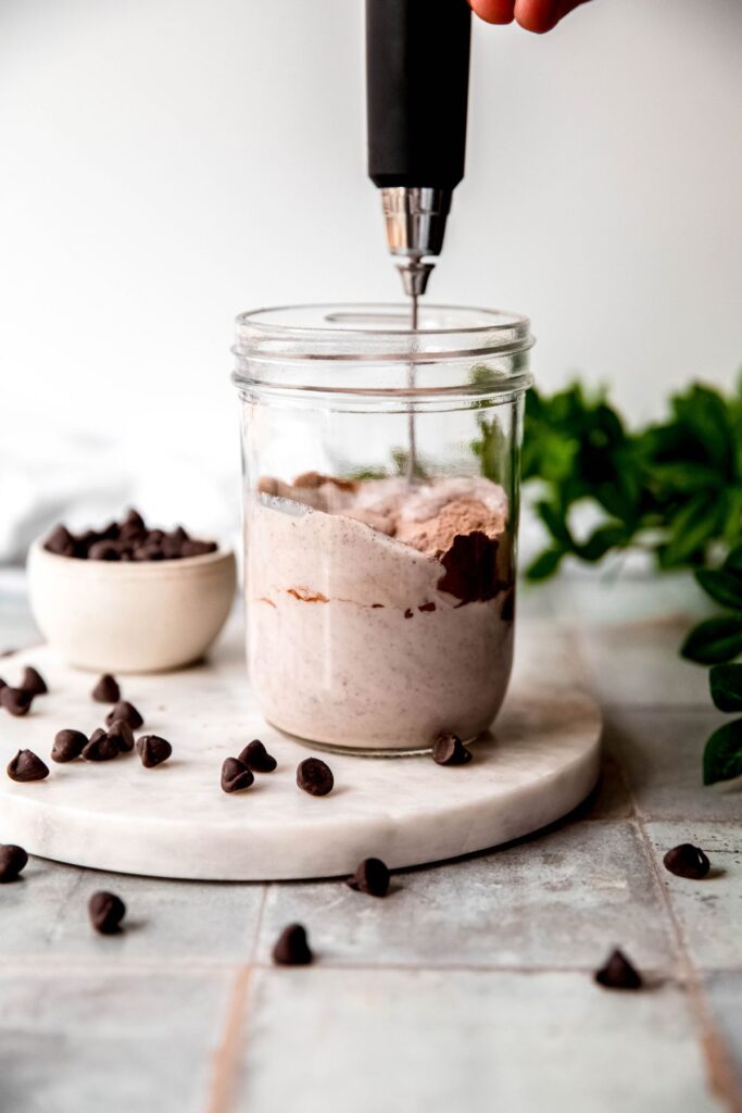 action shot of a milk frother being used to lend the protein powder, maple syrup, cocoa powder, and vanilla extract.