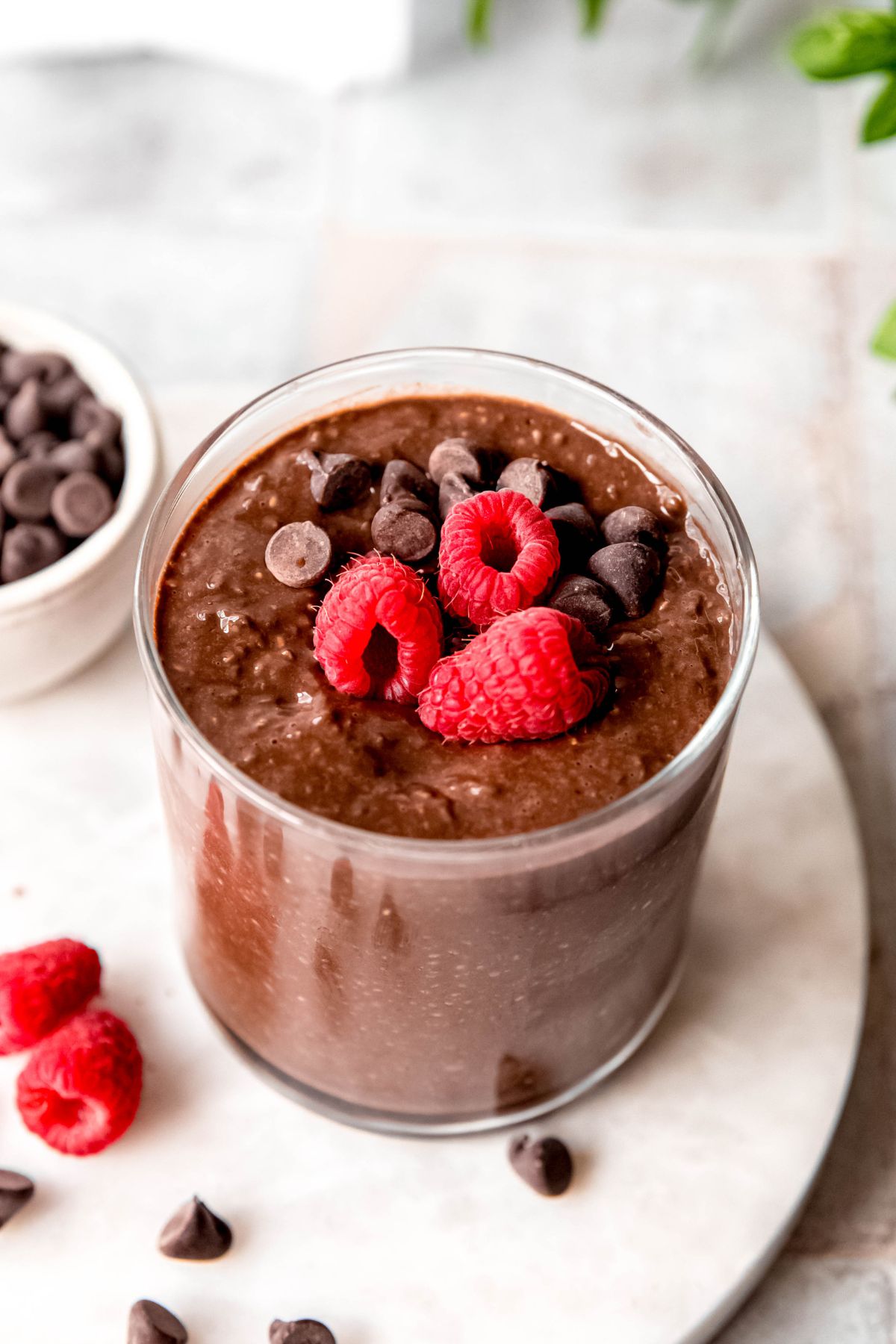 45 degree angle downward closeup shot of a glass filled with high protein chocolate and chia seed pudding topped with fresh raspberries and chocolate chips.