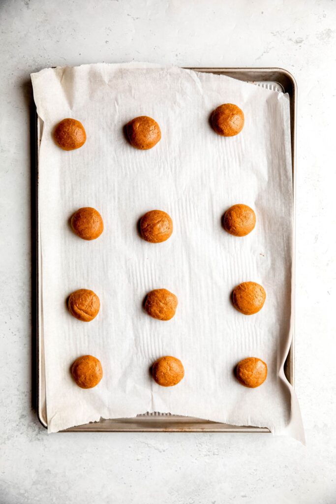 The peanut butter blossom batter rolled into balls on a baking sheet.