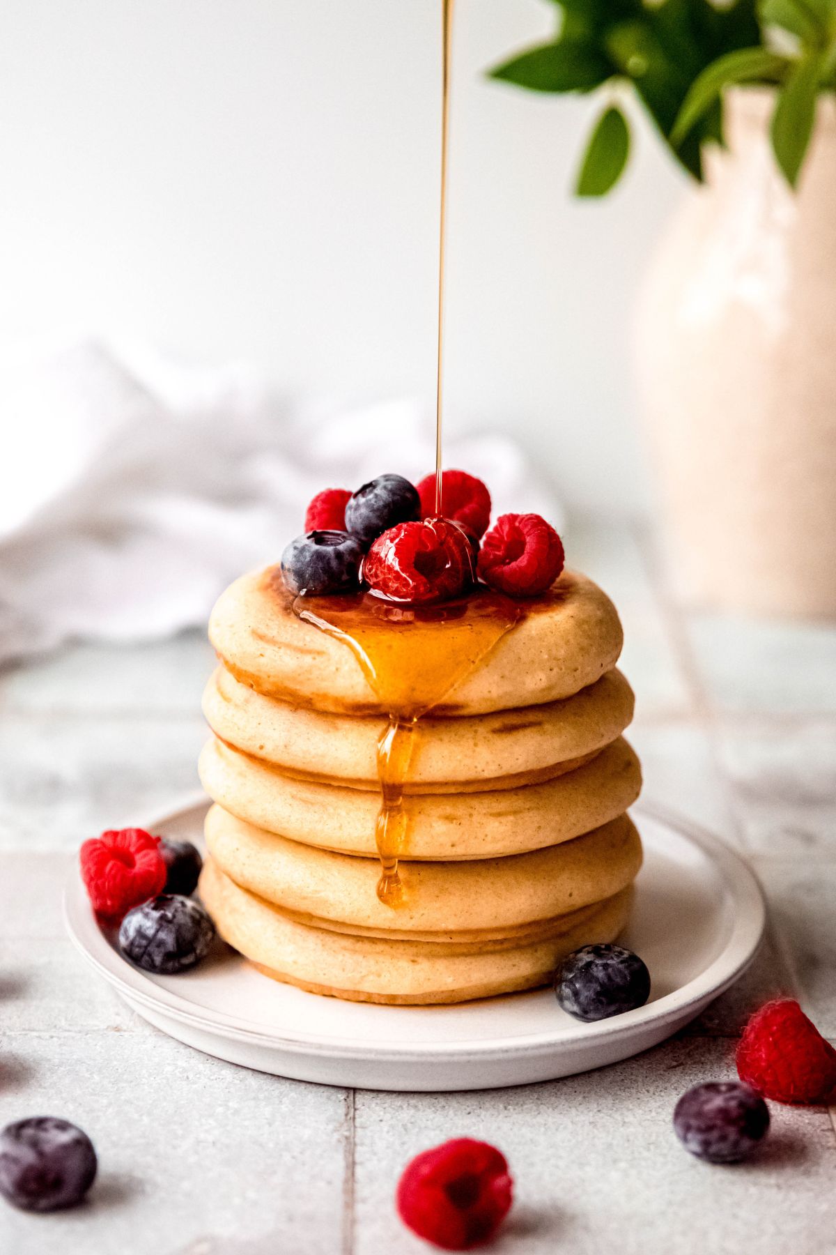 action shot of a stack of protein powder pancakes being drizzled with maple syrup; you can see the syrup running down the side of the stack.