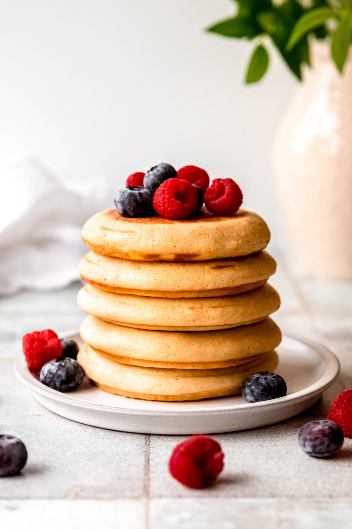 side on view of a stack of fluffy protein pancakes topped with fresh berries; you can see how thick and springy the pancakes are.