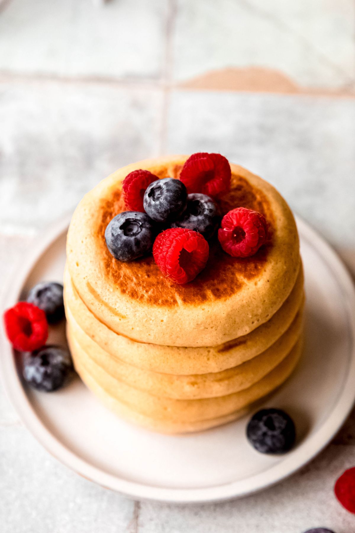 closeup 45 degree angle overhead shot of a stack of high protein pancakes on a white plate topped with fresh berries.