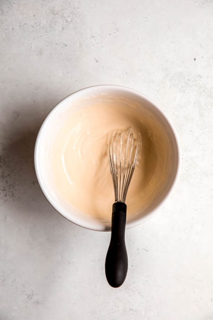 small bowl filled with cream cheese glaze with a black whisk.