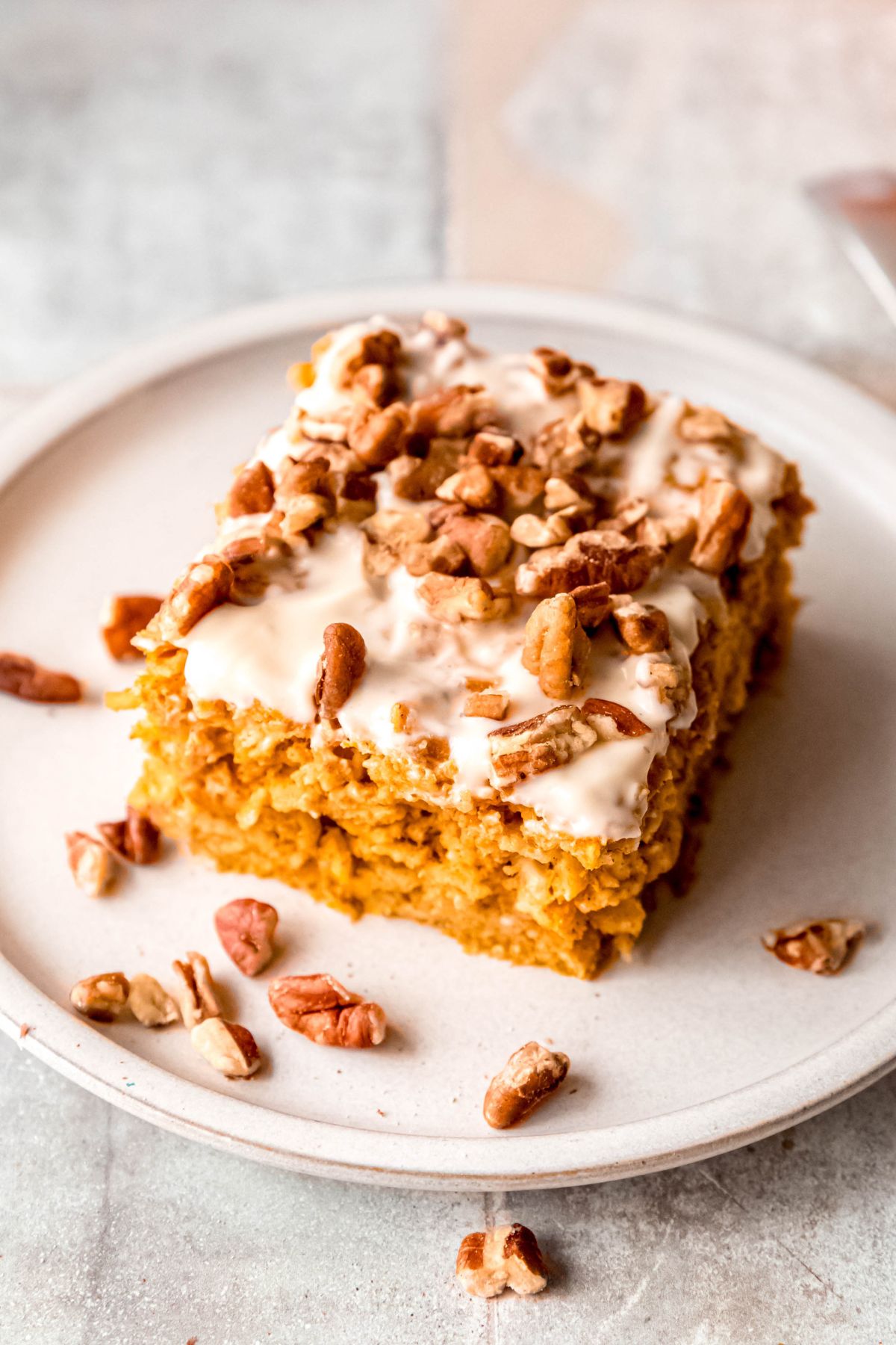 45 degree overhead shot of a slice of high protein baked pumpkin oatmeal with cream cheese glaze and pecans; it looks like a slice of cake!