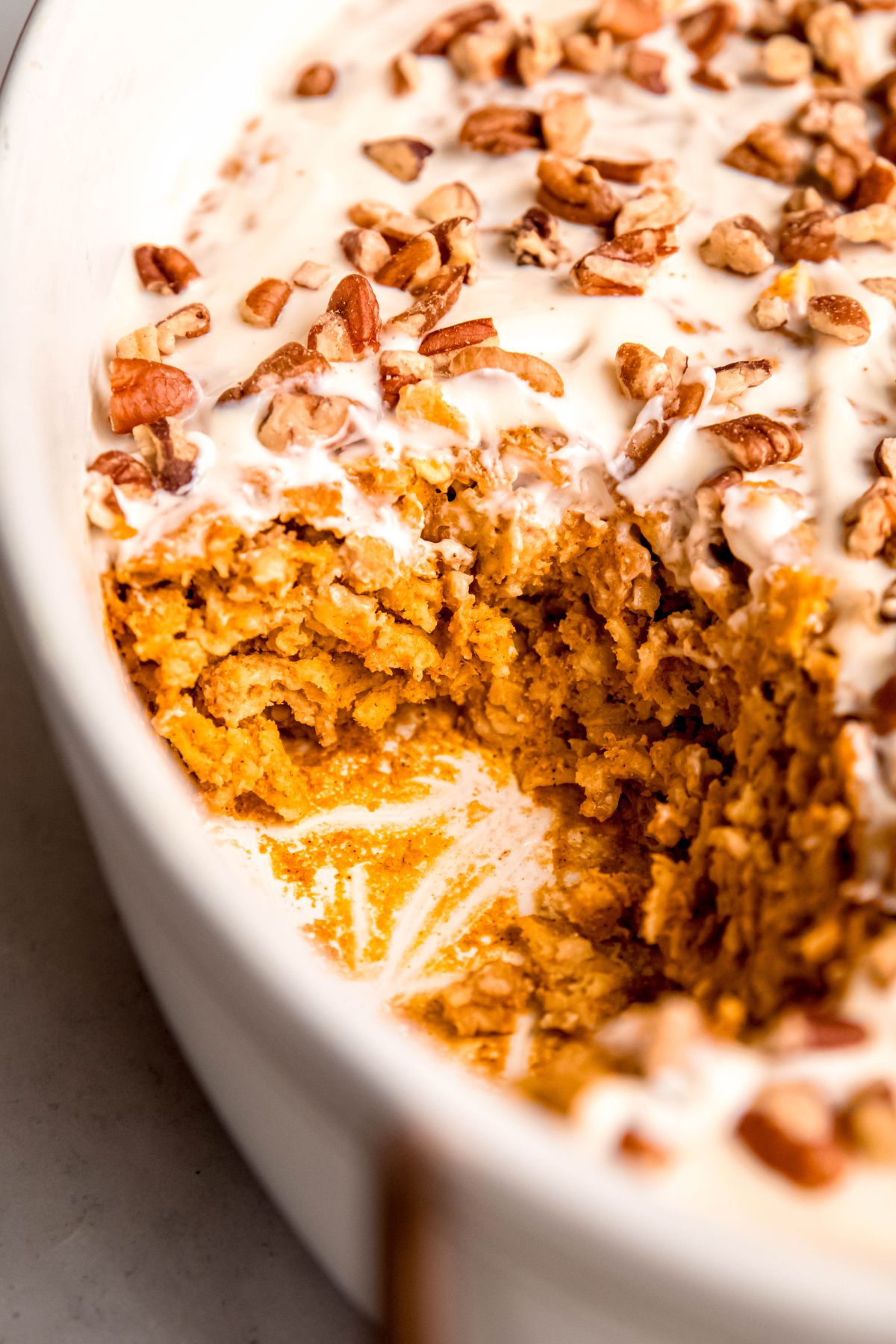 closeup shot of a casserole dish of high protein pumpkin spice baked oatmeal with a slice removed; you can see the cakey texture of the oats and the creamy glaze on top.