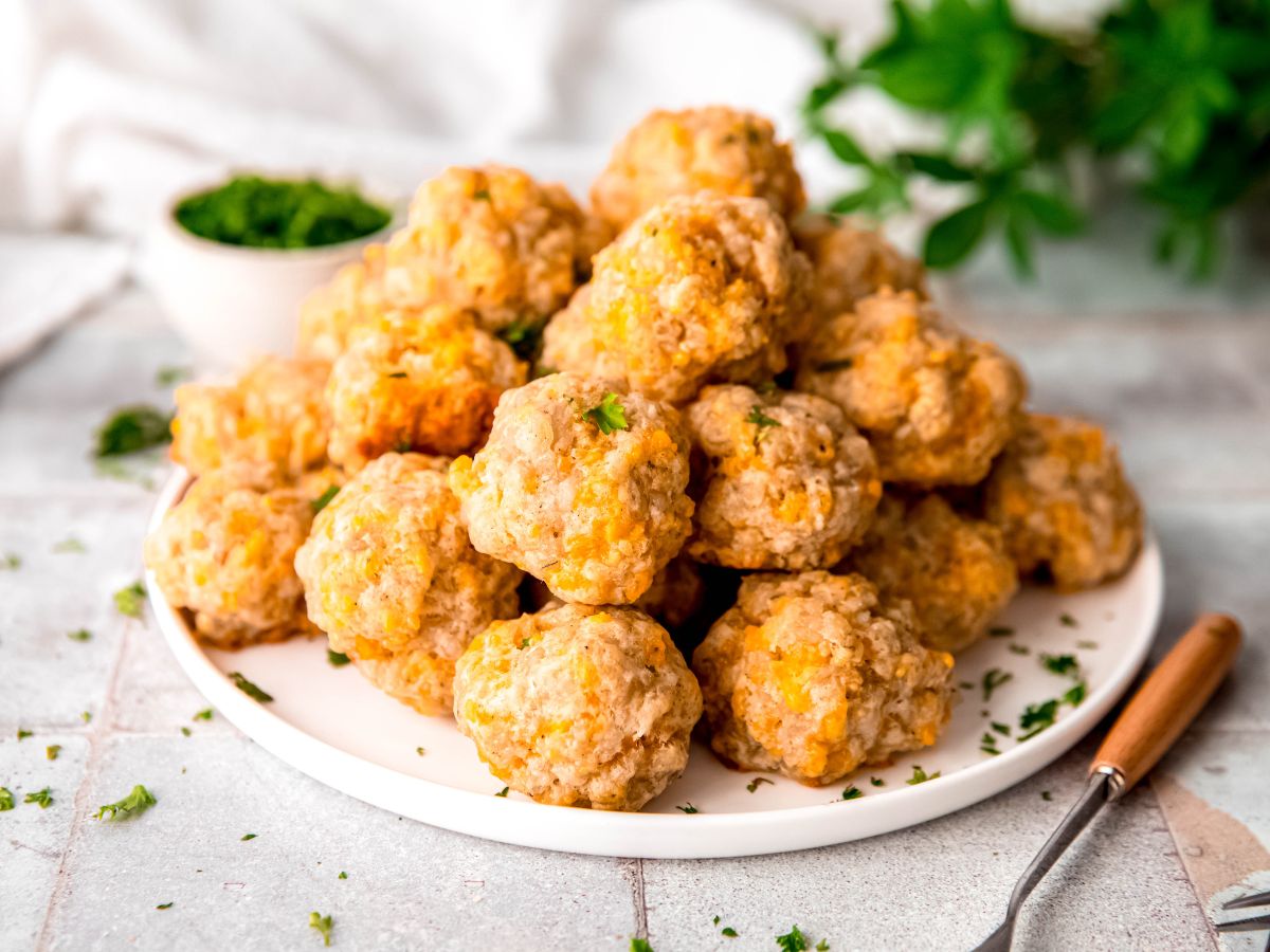horizontally framed hero image of a white plate filled with a stack of sausage balls next to some appetizer forks.