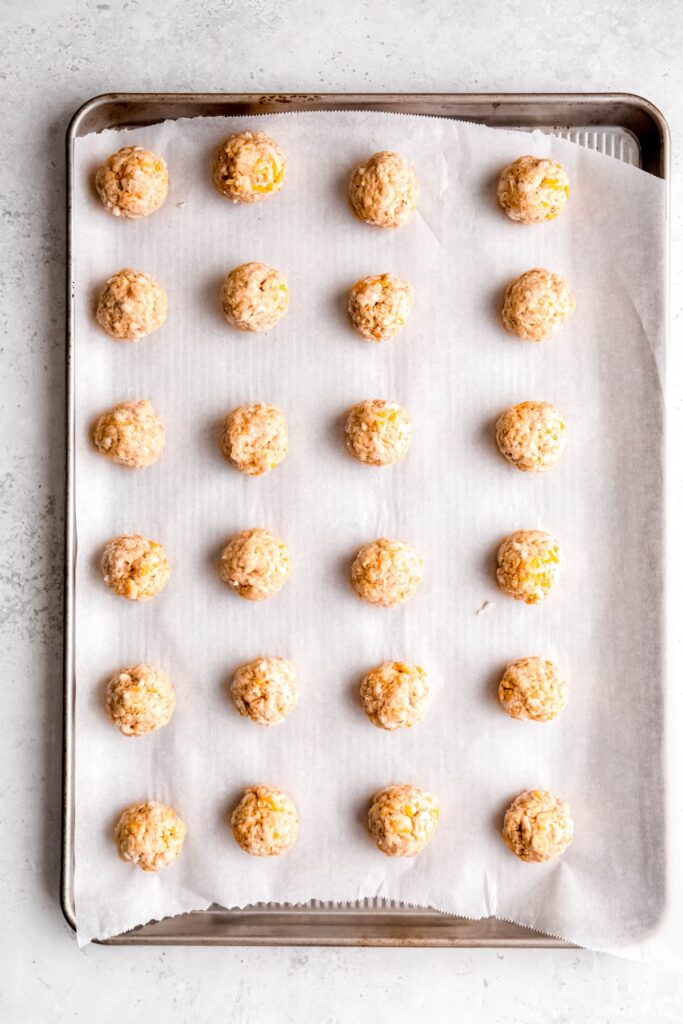 24 raw sausage balls on a parchment lined baking sheet.