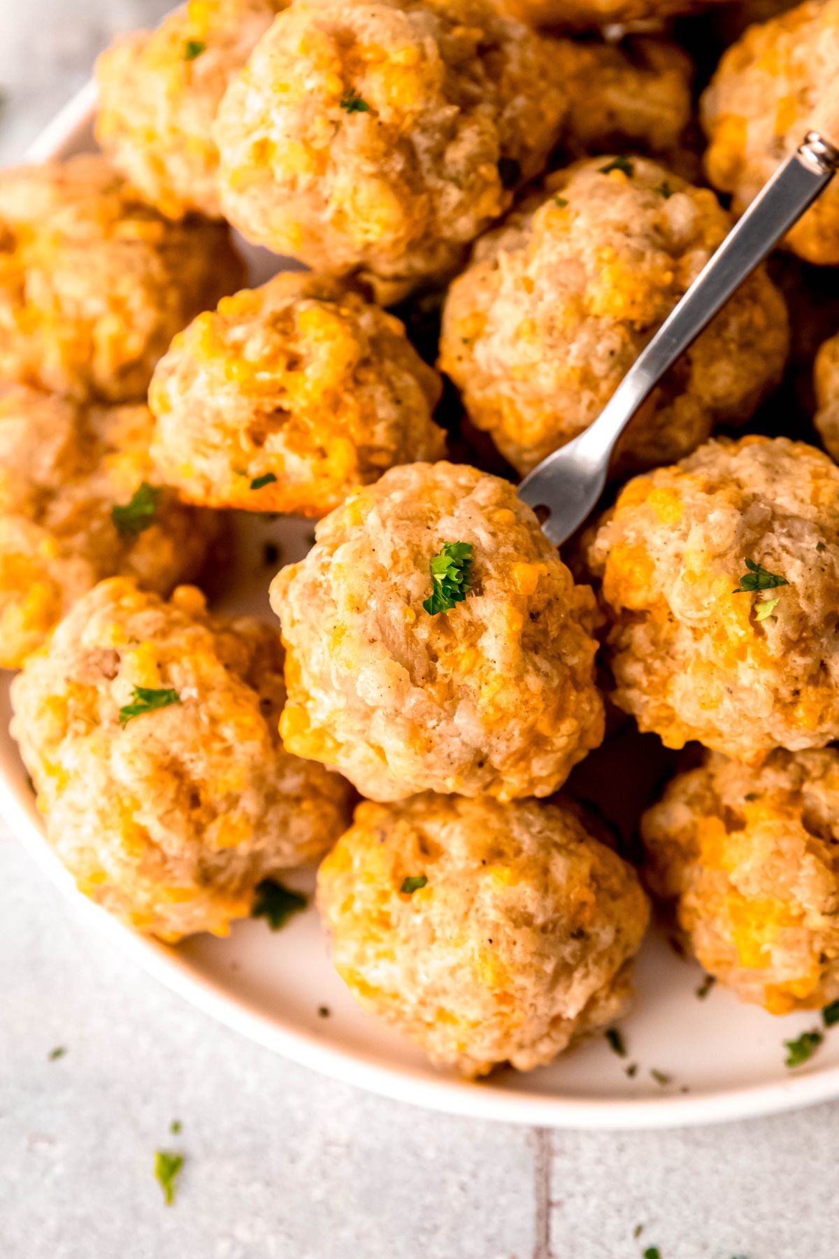 overhead shot of a sausage ball speared on an appetizer fork on the top level of a stack of balls on a plate.