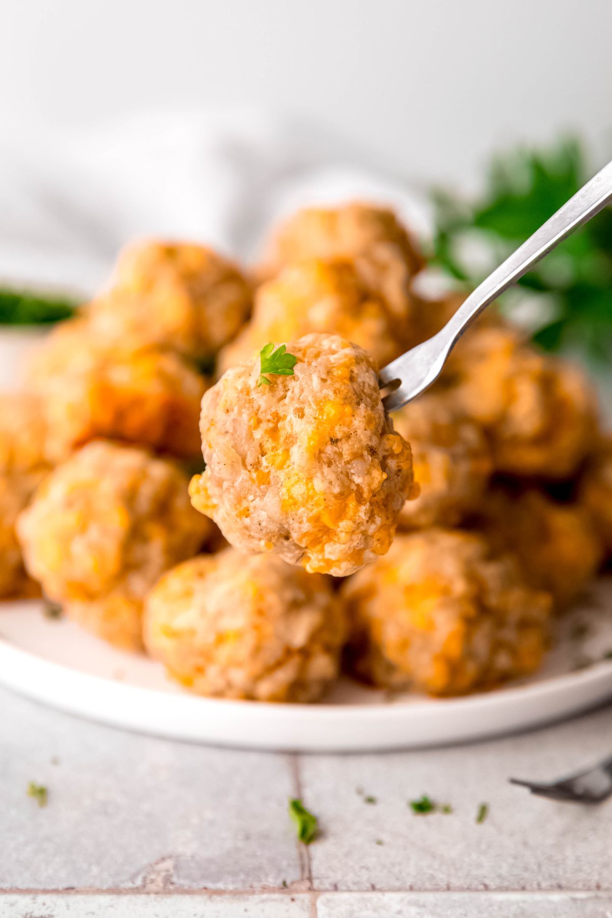 silver appetizer fork with a sausage cheese ball speared on it in front of the plate with the remaining balls blurred out in the background.